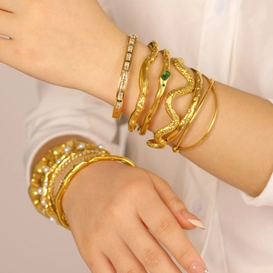 Detailed view of layered gold bracelets with serpent texture and green gemstone on model
