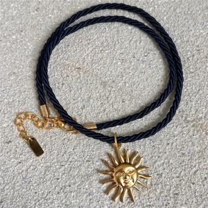 Dettaglio del ciondolo con sole dorato su una catena a corda intrecciata blu scuro e chiusura