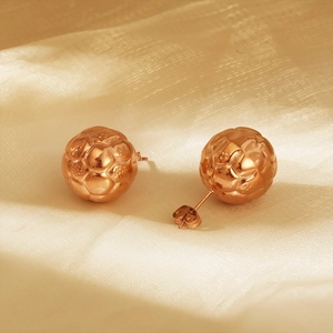 Pair of rose gold hollow football stud earrings on a beige silk fabric background