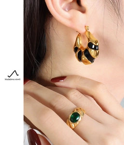 Close-up of gold stainless steel C-shaped earrings with black enamel and green stone ring