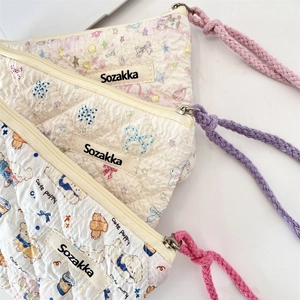 Close-up of three quilted floral cosmetic pouches with woven straps and metal zippers