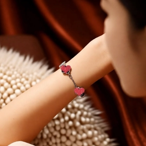 Detailed view of red enamel heart charms on a silver metal bracelet on wrist