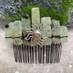 Macro detail of natural green crystal hair comb with silver sun totem on mossy background