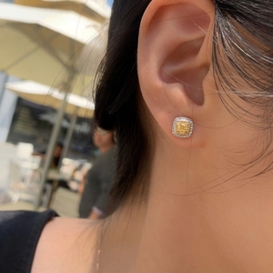 Elegant yellow cushion-cut halo stud earrings worn by a model in natural light