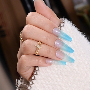 Detail of long gradient press-on nails from nude to blue with subtle glitter and star ring