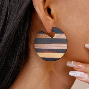 Detail of vintage geometric wood hoop earrings with striped texture on a female model