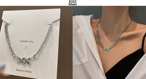 Detail view of silver Cuban chain necklace featuring minimalist X-shaped cross pendant
