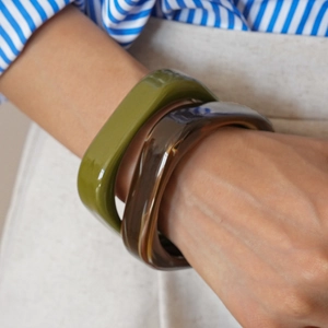 Close-up of olive green and amber resin bangle bracelets worn with a casual outfit