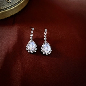 Detailed close-up of silver drop earrings with clear crystals on dark fabric