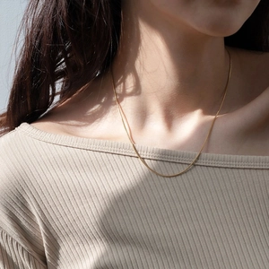 Nahaufnahme einer minimalistischen goldenen Schlangenkette am Hals.