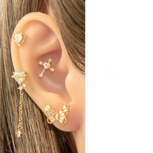 Detail view of heart-shaped ear studs and butterfly piercing jewelry in gold finish