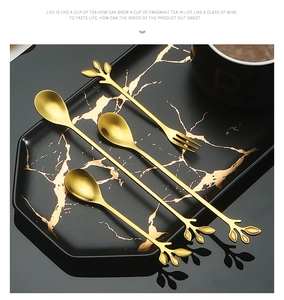 Macro shot of gold leaf-shaped stainless steel dessert spoons and fruit fork on a tray