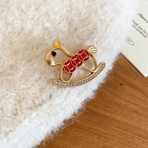 Detailed macro of a rocking horse brooch with red enamel and crystals on white knit fabric
