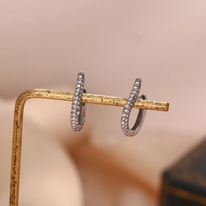 Macro shot of silver J-shape earrings with inlaid white zircons on a golden display stand