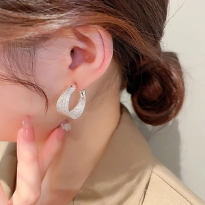 Close-up of a silver multi-layered textured C-shaped hoop earring on a model ear