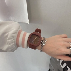 Detail of square quartz watch with red silicone strap and decorative chain bracelet