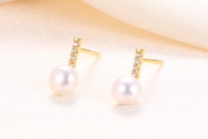 Detailed close-up of gold S925 silver pearl earrings with sparkling zircon row on satin