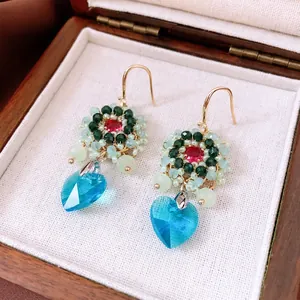 Ethnic beaded flower earrings with blue heart crystal pendants on wooden jewelry box