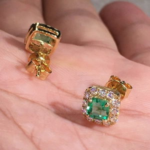 Macro shot of square emerald halo stud earrings in yellow gold plating held in hand