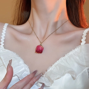 Close-up of golden necklace with a real red dried rose pendant on a female model