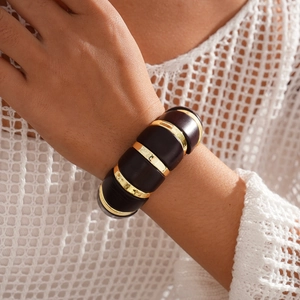 Détail du bracelet élastique avec segments ovales en métal doré poli et résine foncée