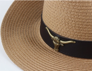 Detail of straw cowboy hat featuring brown leather band and golden bull head ornament