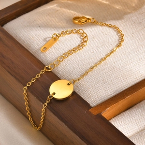 Detail of gold stainless steel bracelet with blank round pendant on wooden tray
