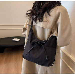 Detail of black suede hobo bag with ribbon bow knot and metal buckle on wide shoulder strap