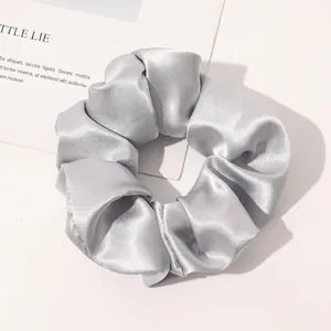 Macro detail of silver-grey silk satin scrunchie with soft sheen on white background