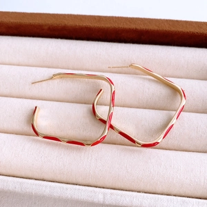 Detailed view of wavy square gold earrings with red enamel on a soft jewelry tray