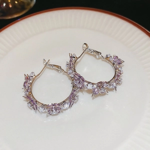 Macro detail of silver needle butterfly C-shaped earrings with purple zircon in a ceramic dish