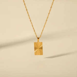 Macro shot of gold sunburst rectangular pendant with a twisted chain on beige backdrop