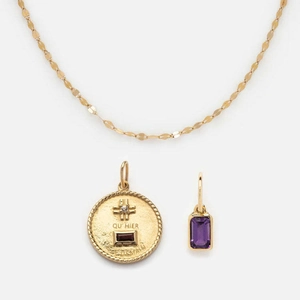 Detail of gold necklace featuring an engraved coin pendant and a purple zircon stone charm