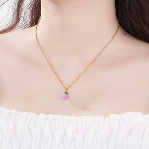 Detailed view of a purple strawberry pendant on a gold chain worn by a model