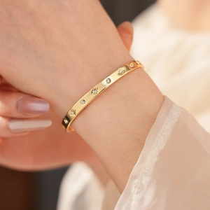 Détail d'un bracelet doré avec gravures d'étoiles et accents de zircones ronds