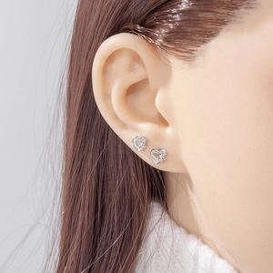 Elegant silver heart stud earrings with sparkling cubic zirconia on female model's ear