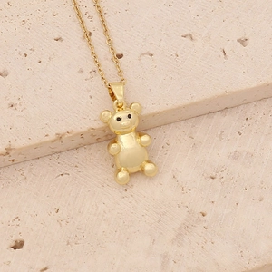 Close-up of a gold teddy bear pendant necklace with zircon on a beige stone surface