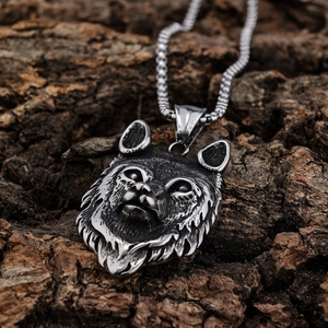 Close-up of a textured wolf head pendant on rough bark background showing metallic detail