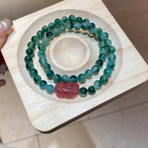Close-up of green agate beads and red PiXiu charm on a rustic wooden tray