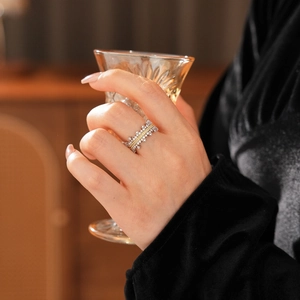 Detail of a crown-shaped bicolor zircon ring worn while holding a vintage glass cup