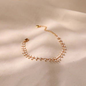 Detail shot of a bohemian gold chain bracelet with delicate white beads on beige fabric