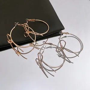 Polished gold and silver hoop earrings with 3D bowknot accents on a reflective surface