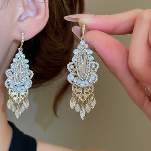 Close-up of gold tassel earrings with light blue crystals and hollow patterns