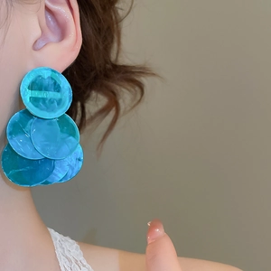 Close-up of layered blue circular shell fringe earrings worn by a model for beach style