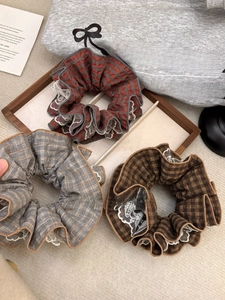 Detailed view of large plaid scrunchies with white lace edges in red, gray and brown
