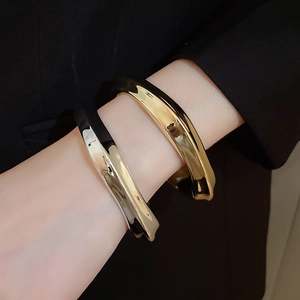 Gros plan de bracelets torsadés en métal doré et argenté portés sur un costume sombre
