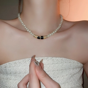 Gros plan d'un tour de cou vintage en perles avec pendentif émaillé noir et strass
