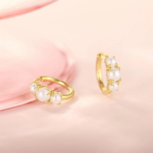 Close-up of gold hoop earrings featuring three elegant white pearls on a pink surface