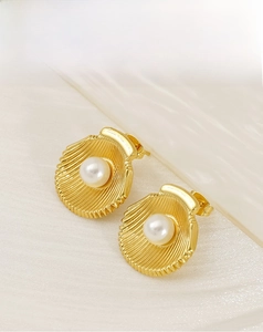 Close-up of gold shell stud earrings with white pearls on a soft silk background