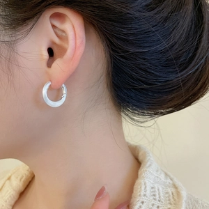 Close-up of minimalist brushed white round hoop earrings worn by a model